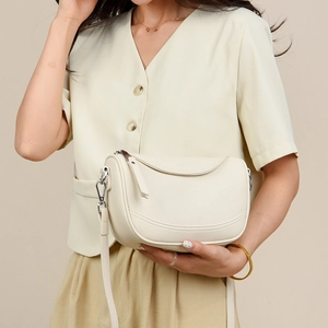 Close-up of beige saddle bag showing lychee pattern leather and metal hook detail