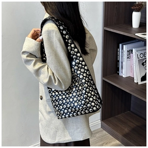 Detail of black leather bucket bag with silver metal rivets worn by a model