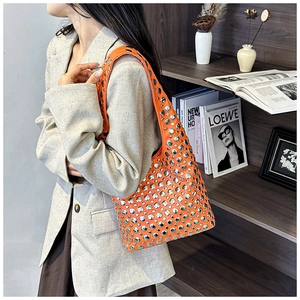 Detail of bright orange crossbody bag featuring silver metal studs and wide shoulder strap