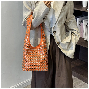 Close-up of vibrant orange handbag with silver rivets worn over the shoulder as a stylish accessory