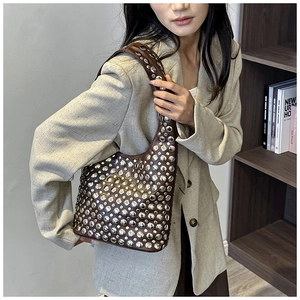 Close-up of brown leather shoulder bag with silver rivet details worn by model