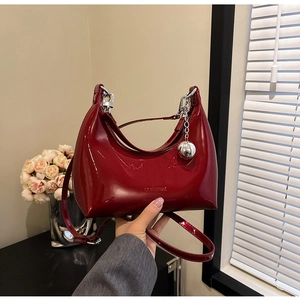 Close-up of a wine red patent leather handbag with a silver ball charm and metallic finish