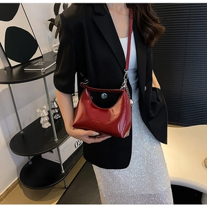 Detail view of red glossy patent leather crescent bag styled with a sleek metal chain