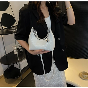 Close-up of a white patent leather crescent bag with silver chain and metal ball charm
