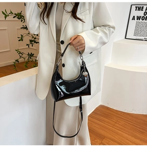 Detail of black patent leather hobo bag featuring silver hardware and a metallic ball charm