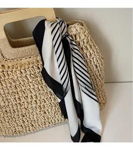 Detail of a silky black and white geometric scarf tied to a woven straw bag handle