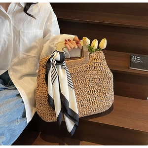 Detail of woven straw tote bag with curved handle and decorative striped scarf on stairs