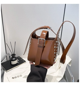 Détail du sac seau en cuir marron avec clous argentés et boucles métalliques de style chic