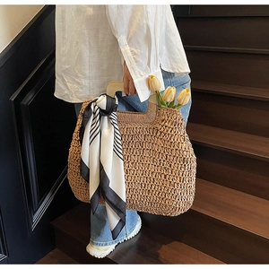 Close-up of woven straw beach bag featuring wooden handle and striped scarf detail