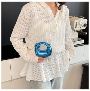 Detail of blue metallic hollow sphere handbag with fine golden chain strap over white shirt