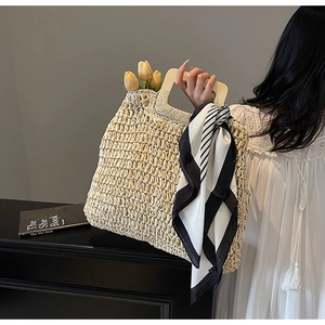 Detail of woven straw tote bag featuring square wood handles and a striped silk scarf