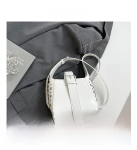 Détail d'un sac en cuir blanc avec rivets argentés et boucle sur un tissu de costume gris