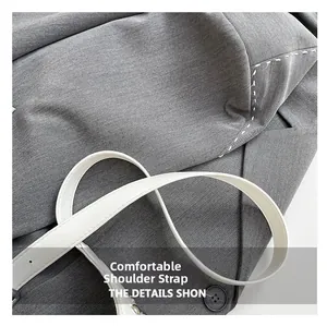 Détail d'une bandoulière en cuir blanc sur un sac à main gris avec des rivets métalliques