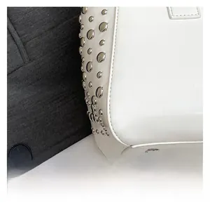 Détail du sac seau en cuir blanc avec des clous ronds argentés et des pieds de protection
