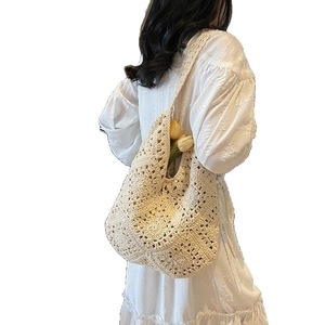 Cremefarbene Häkeltasche mit Blumenmuster an Model in weißem Kleid getragen