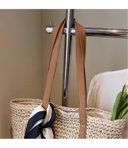 Detail of hand-woven straw tote bag with brown leather handles and striped silk scarf