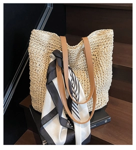 Detailed texture of hand-woven straw tote bag with brown leather straps and striped scarf