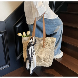 Close-up of woven straw tote bag featuring brown leather handles and striped silk scarf detail