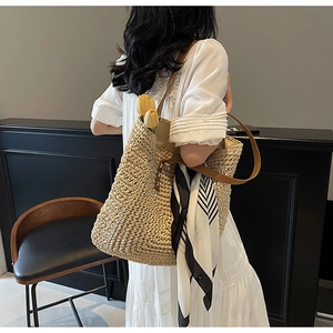 Detailed view of a woven straw tote bag featuring brown leather straps and a printed silk scarf