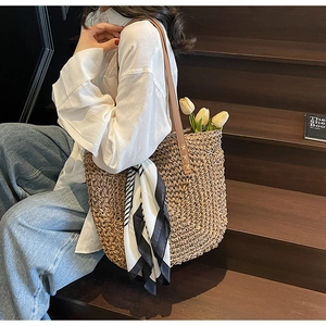 Detail of woven straw tote bag featuring leather handles and a striped silk scarf accessory