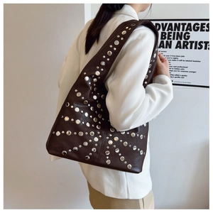 Detailansicht einer großen braunen Shopper-Tasche mit silbernen Nieten und breitem Gurt