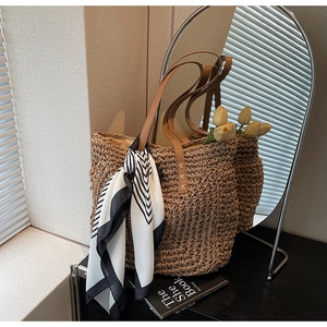 Detail of woven straw tote bag featuring brown leather straps and geometric silk scarf