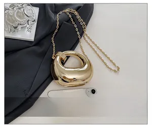 Detail of gold crescent evening bag with metallic finish and chain next to a phone
