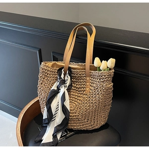 Detail of woven straw tote bag with leather handles and decorative silk scarf
