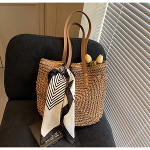 Close-up of woven straw tote bag featuring leather handles and a decorative striped scarf