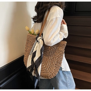 Detail of large straw tote bag with brown leather shoulder strap and striped scarf decor