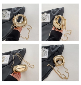 Detail of a high-shine gold oval clutch bag with round top handle and metal chain strap
