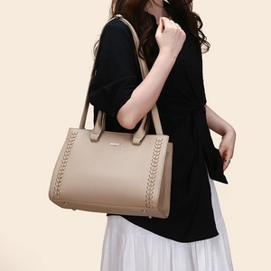 Detail of beige litchi leather tote bag with braided accents on a female model