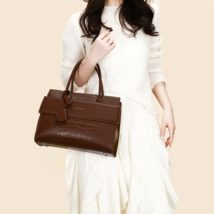 Detail of dark brown crocodile embossed leather handbag with metallic hardware and top handles