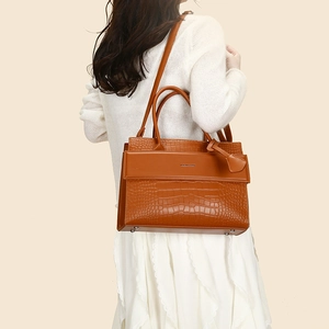 Detail of a brown crocodile pattern leather handbag shown on a model for size perspective