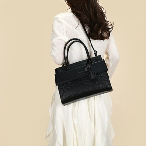 Detail of black crocodile embossed tote bag with detachable shoulder strap worn by a model