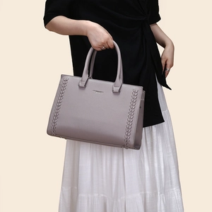 Close-up of taupe tote bag with litchi grain leather texture and woven side details