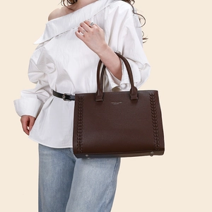 Detail of dark brown leather tote bag with woven side texture and gold bottom studs