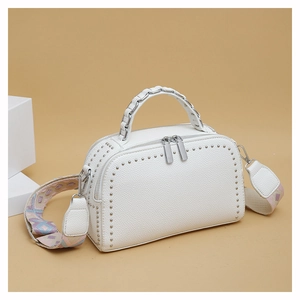 Close-up of white lychee leather bag with silver studs and woven geometric shoulder strap