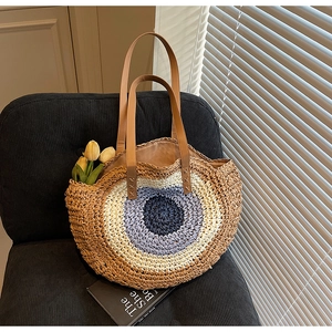 Handmade woven straw beach bag with evil eye design and brown leather straps on chair