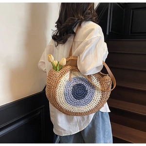 Macro detail of round woven evil eye shoulder bag with brown leather strap and straw texture