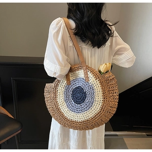 Macro view of woven straw shoulder bag with evil eye design and brown leather strap