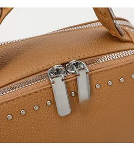 Detail of silver dual zippers and round rivets on caramel pebbled leather handbag