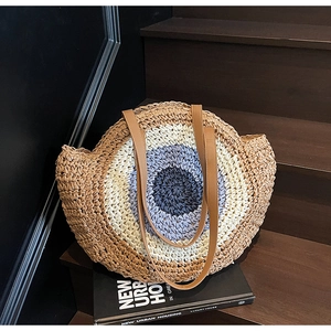 Close-up of circular hand-woven straw bag with colorful gradient pattern and leather strap
