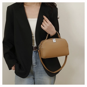 Brown leather boston bag with silver stud accents worn by a model in a stylish outfit