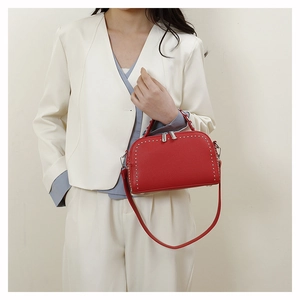 Detail of red pebbled leather crossbody bag with silver rivets held by a model