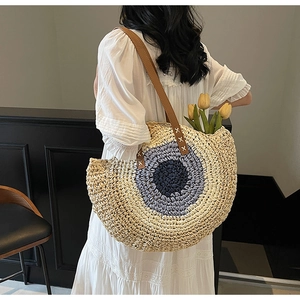 Detailed view of woven straw beach bag with blue evil eye pattern and leather strap