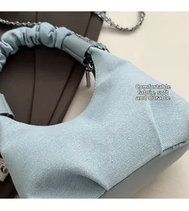 Close-up of light blue denim cloud bag featuring a ruched handle and silver chain strap