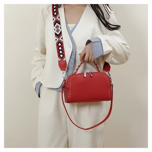 Detail of red crossbody bag featuring silver rivet trim and geometric patterned strap
