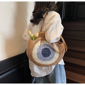 Detail of round woven straw bag with blue contrast patterns and leather shoulder strap