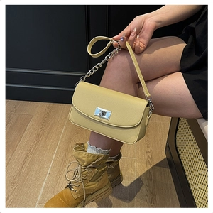 Detail of yellow pebbled leather handbag with silver twist lock and decorative metal chain